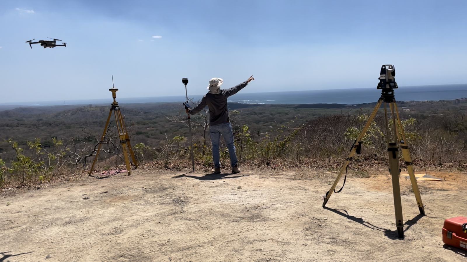 Equipo de campo con dron en vuelo y receptores GNSS sobre trípodes en un cerro